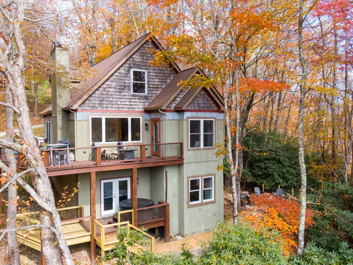 An expansive wooden deck with seating, set against a backdrop of vibrant autumn foliage and large windows. The deck’s proximity to the indoor living area hints at indoor-outdoor flow, with opportunities for outdoor dining and mountain views.