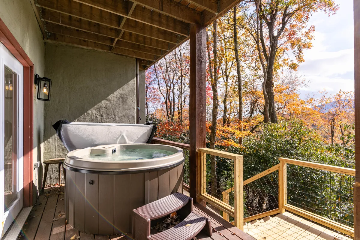 An inviting outdoor deck area with a bubbling hot tub set among tall trees. The hot tub is positioned for scenic views and relaxation, suggesting a peaceful retreat after a day of adventure. The surrounding greenery creates a tranquil, rejuvenating atmosphere.