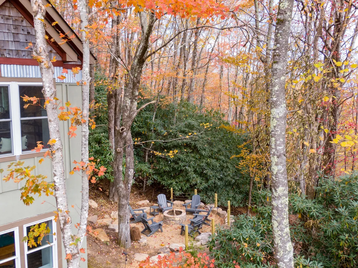 A cozy firepit area surrounded by adirondack chairs and vibrant autumn foliage. The setup encourages gathering, storytelling, and making s’mores under the stars, creating an inviting communal space for evening enjoyment.