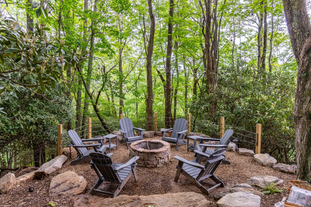 A cozy outdoor fire pit encircled by Adirondack chairs, nestled among tall trees. The area feels communal and relaxed, perfect for winding down after a day of outdoor activities.