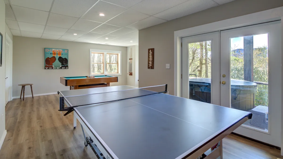 A lively interior rec room featuring a ping pong table, pool table, and large windows that let in natural light. Artwork on the wall and ample space suggest a fun, welcoming environment for friendly competition and group activities.